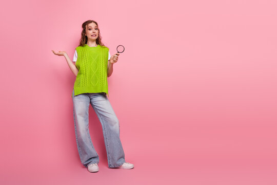 Young female student in bright vest poses with magnifying glass against pink background for fashion lifestyle image