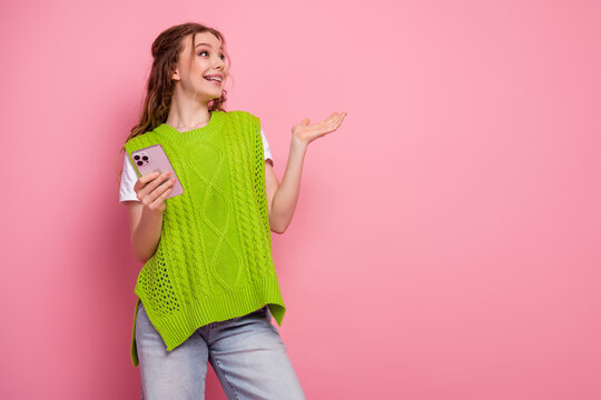Young woman in bright green vest smiles while using phone against pink background