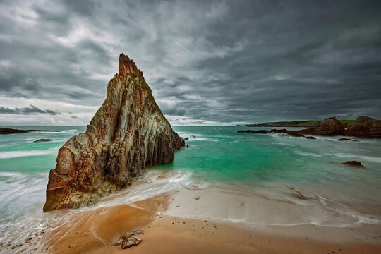 Sharp, central rocky islet midway along Playa de Mexota-A Mixota Beach, at rising tide in a cloudy yet spectacular spring sunrise. Asturias-Spain-011