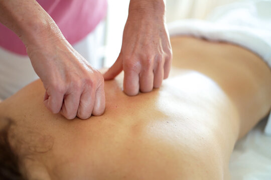 Therapist performing deep tissue back massage on adult male client in bright treatment room with natural light, focused pressure on muscles, calm wellness care and recovery setting