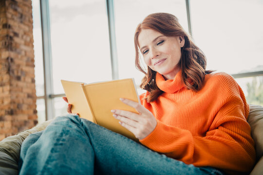 Young woman reading a book at home in a cozy orange sweater, relaxed lifestyle and quiet leisure by a sunny window