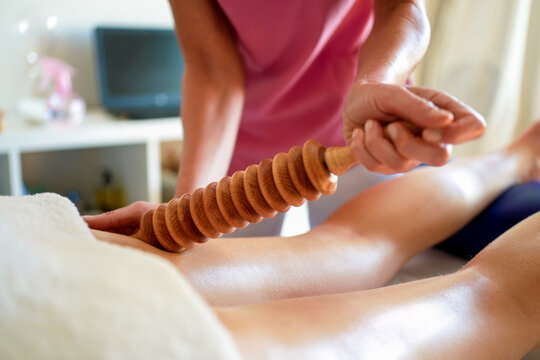 Therapist using wooden roller for lower leg massage and muscle relief during wellness treatment in warm spa room, with massage, therapy, wellness, roller detail
