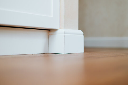 A quarter view shows a white baseboard with a decorative corner piece next to a cabinet.