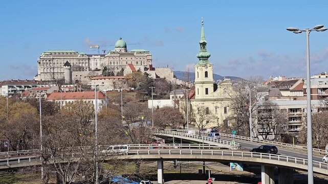 Buda Castle above Taban rooftops, Budapest, Hungary, a baroque church spire and road flyovers below the palace in clear winter light