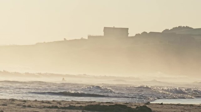 Backlit surf breaks below a clifftop house at Oyambre, Cantabria, Spain