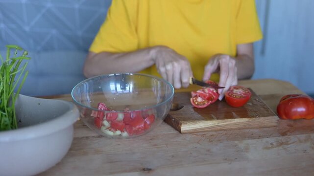 Woman's hands slicing fresh red tomatoes on wooden cutting board and putting them into glass bowl for vegetable salad