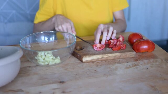 Woman's hands slicing fresh red tomatoes on wooden cutting board and putting them into glass bowl for vegetable salad