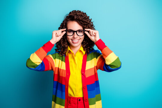 Smiling young woman in rainbow cardigan and glasses against a turquoise background, cheerful studio portrait conveying confidence, colorful fashion, playful style and positive modern vibe