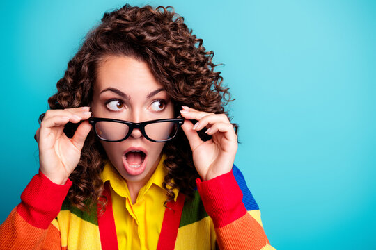 Surprised young woman with glasses looking to the side wearing a colorful striped sweater against a turquoise background