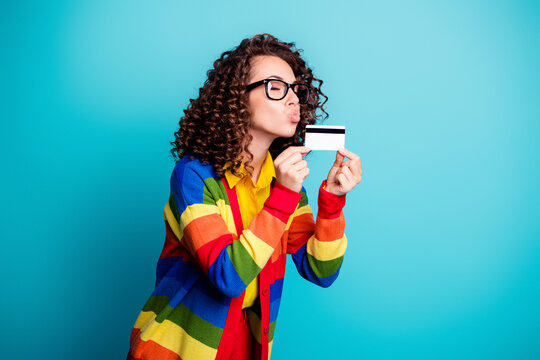 Young woman in rainbow sweater kissing a credit card, joyful consumer holding bank card and celebrating shopping and payment freedom