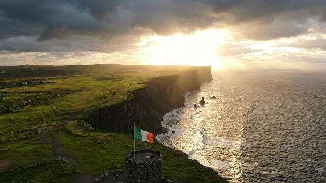 Aerial view of cliffs of moher at sunset with irish flag waving over o'brien's tower, ireland travel landmark