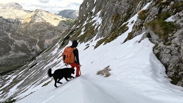 Solo male hiker with a dog on a dangerous mountain trail climbing down a large snowfield wearing crampons in Durmitor National Park in Montenegro