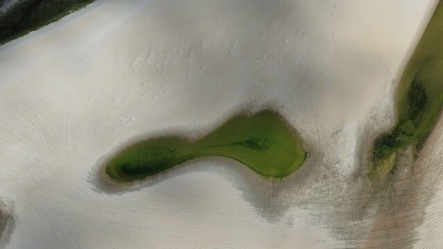 Aerial view of a vibrant green lagoon nestled within the vast white sand dunes of Parque Nacional dos Lencois Maranhenses, Atins, Maranhao, Brazil.