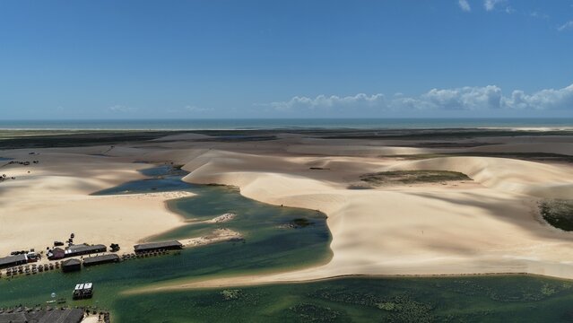 Aerial view of the vast sand dunes and seasonal lagoons of Parque Nacional dos Lencois Maranhenses with small structures near the water in Atins, Maranhao, Brazil.
