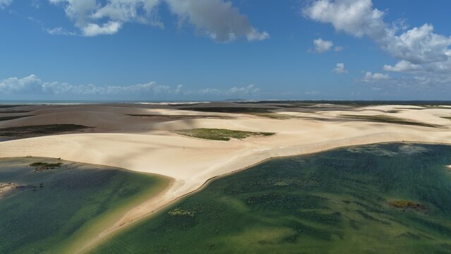 Aerial view of Parque Nacional dos Lencois Maranhenses featuring vast white sand dunes and vibrant green lagoons under a clear blue sky in Atins, Maranhao, Brazil.