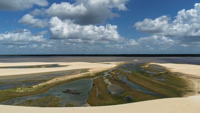 Aerial view of Parque Nacional dos Lencois Maranhenses featuring white sand dunes and seasonal lagoons under a blue sky with clouds in Atins, Maranhao, Brazil.