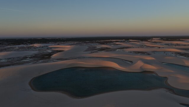 Aerial view of Parque Nacional dos Lencois Maranhenses with its vast white sand dunes and crystal clear lagoons under the golden hour light in Atins, Maranhao, Brazil.
