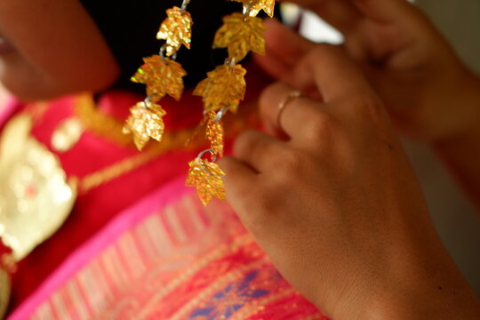 Hands adjusting traditional golden ornament on red ethnic wedding dress