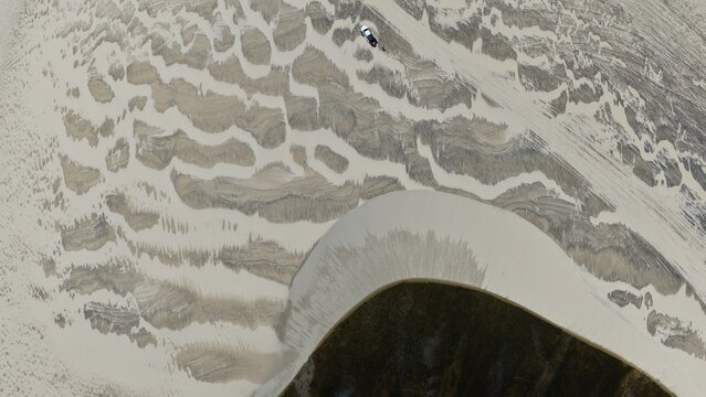 Aerial view of Parque Nacional dos Lencois Maranhenses featuring vast white sand dunes with intricate patterns and a small vehicle parked on the sand in Atins, Maranhao, Brazil.