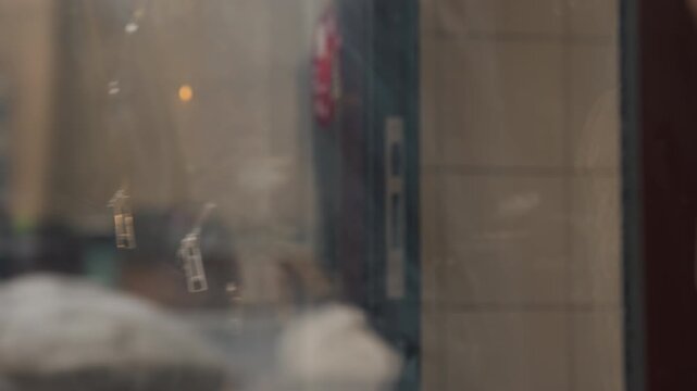 Close up of glass door with wooden frame and metal handle reflecting winter scene. person in brown coat briefly touches doorknob from outside as camera slowly pans along vertical axis