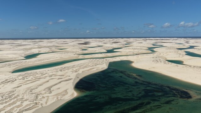 Aerial view of Parque Nacional dos Lencois Maranhenses featuring vast white sand dunes and turquoise lagoons under a clear blue sky in Atins, Maranhao, Brazil.