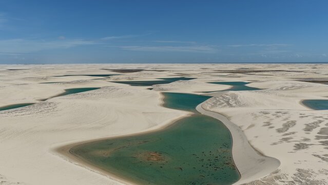 Aerial view of the white sand dunes and turquoise lagoons of Parque Nacional dos Lencois Maranhenses under a clear blue sky in Atins, Maranhao, Brazil.