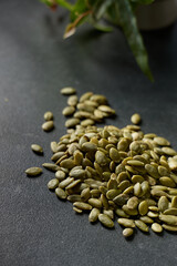 Obraz premium Pumpkin seeds are scattered on a dark surface with a plant in the background