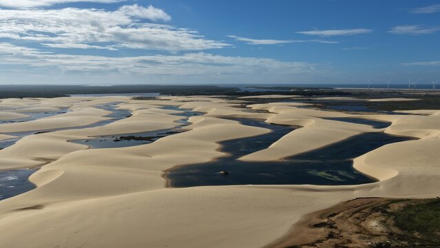 Aerial view of Parque Nacional dos Lencois Maranhenses featuring vast white sand dunes and seasonal rainwater lagoons under a clear blue sky in Atins, Maranhao, Brazil.