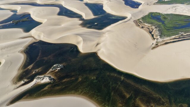 Aerial view of Parque Nacional dos Lencois Maranhenses featuring vast white sand dunes and crystal clear rainwater lagoons under bright sunlight in Atins, Maranhao, Brazil.