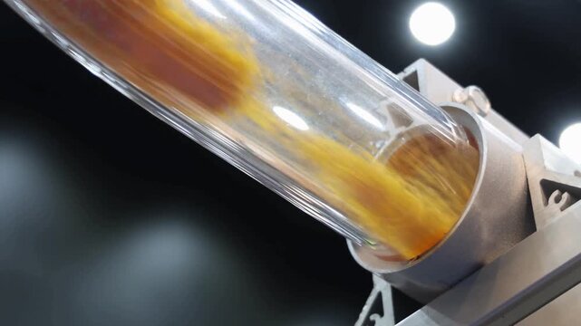 Close up of transparent industrial tube transporting yellow plastic pellets on automated machine, High speed motion engineering material handling.