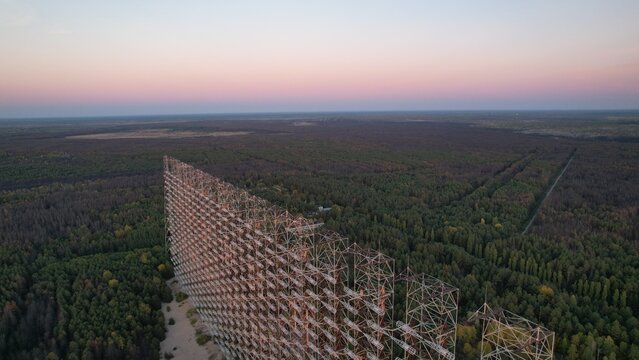 Aerial view of the Duga radar array, a massive Soviet-era radar structure rising above the dense forest canopy in the Exclusion Zone at dusk in Ivankivs'kyi district, Kyiv Oblast, Ukraine.