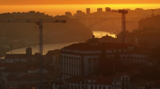 Aerial view of sunset over the city skyline with construction cranes and the Douro River in Porto, Porto District, Portugal.
