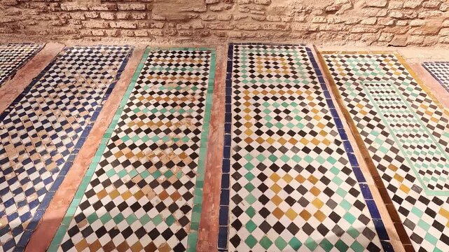 Zellij floor panels at the Saadian Tombs, Marrakech, Morocco, green and blue mosaic below bare brick in soft daylight