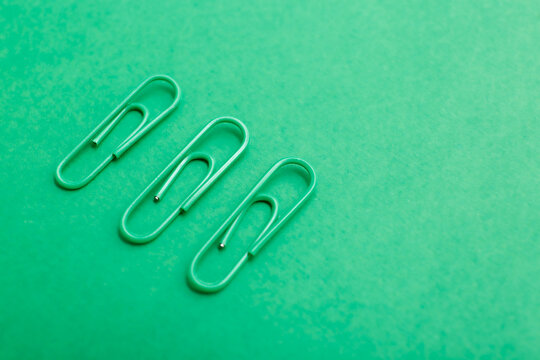 Monochromatic photo of three green paperclips arranged in a horizontal line on a green surface. Minimalist composition highlights repetition, geometry, and stationery.
