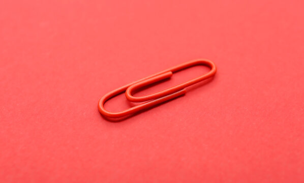 Minimalist photo of a single red paperclip placed vertically on a red surface. Monochromatic composition emphasizes simplicity, stationery, and everyday objects.