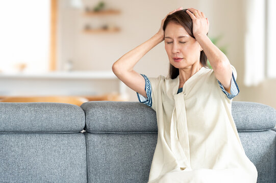 リビングで頭を抱えて辛そうな中高年の女性　体調不良