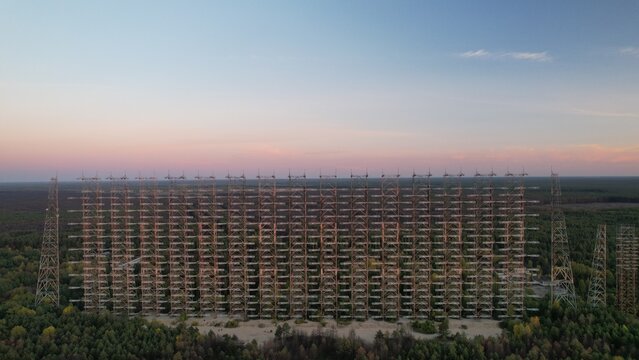 Aerial view of the Duga radar array, a massive Soviet over-the-horizon radar system, rising above the surrounding forest at sunset in Ivankivskyi District, Kyiv Oblast, Ukraine.