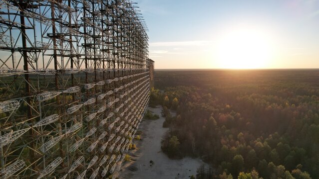 Aerial view of the Duga radar array, a massive Soviet-era over-the-horizon radar system, standing tall above the surrounding forest at sunset in Ivankivs'kyi district, Kyiv Oblast, Ukraine.