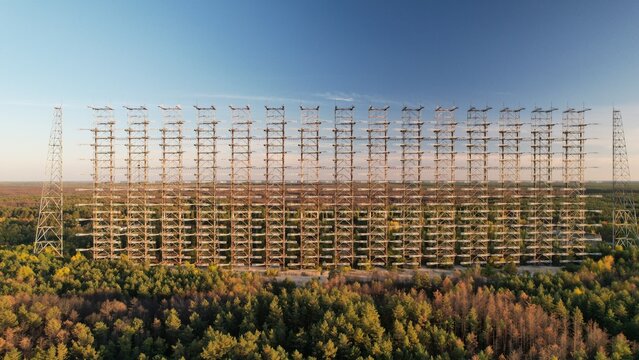 Aerial view of the massive Duga radar array rising above the dense forest canopy under a clear blue sky in Ivankivs'kyi district, Kyiv Oblast, Ukraine.