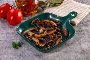 Fototapeta premium Fried sliced mushrooms in a green bowl with fresh tomatoes and herbs on a grey stone background