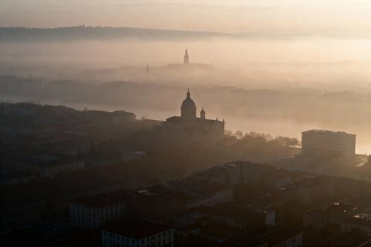 Aerial view of a cityscape enveloped in morning fog with a prominent domed building visible through the mist