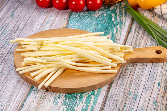 String cheese sticks on wooden cutting board with cherry tomatoes and green onions