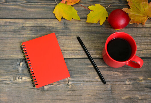 Red Notebook, black pen and Coffee Mug on Wooden Table with Autumn Leaves, flat lay, coffee break
