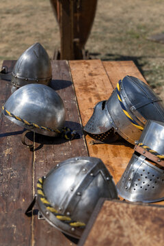 Medieval knight steel helmets displayed on a wooden table during an outdoor historical reenactment.