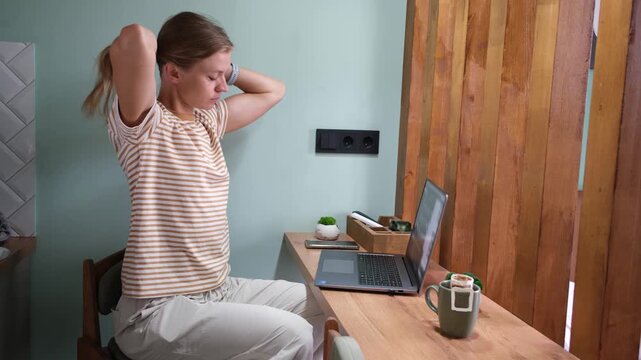 young woman in a stiped shirt working on a laptop at home on the kitchen counter, distant work and education