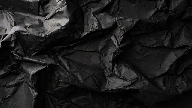 Dark, crumpled paper texture with deep shadows and subtle light highlights