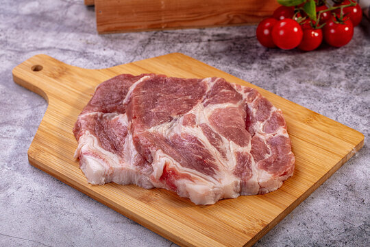 Raw pork neck steak on wooden cutting board with cherry tomatoes background