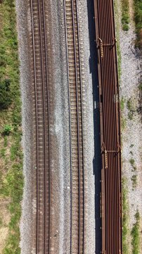 Aerial view of parallel railway tracks and a rusty freight car on gravel ballast with green vegetation in Brazil.