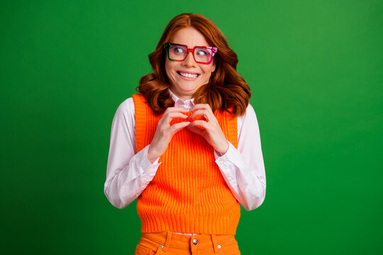 Quirky redhead woman in orange sweater vest and colorful glasses with an awkward excited smile against a green background