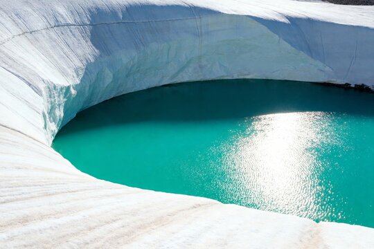 Glacial meltwater pool with turquoise water surrounded by snow and ice